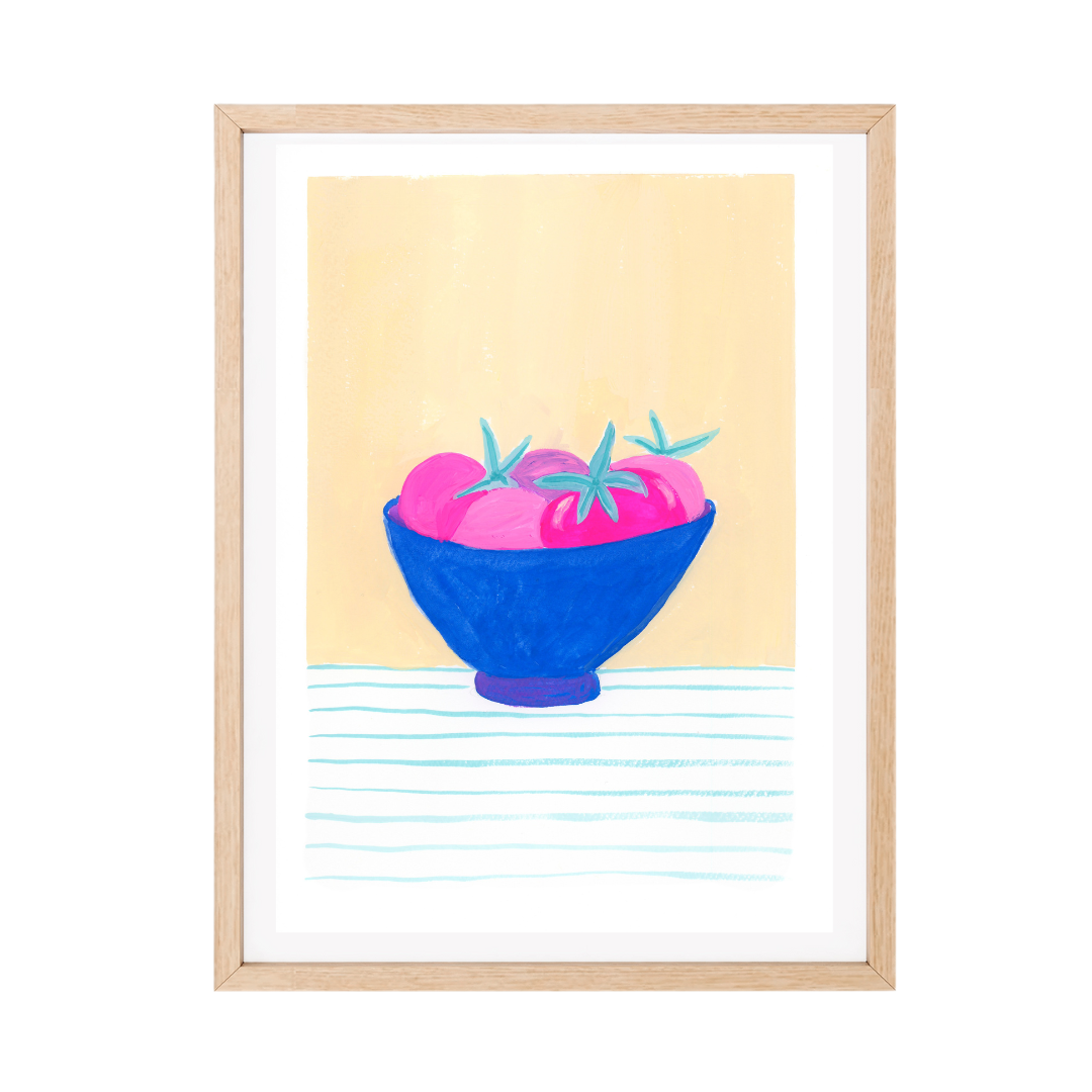 A framed original gouache artwork featuring a still life illustration of pink tomatoes in a blue bowl, set against a pale yellow background with light blue horizontal lines at the bottom. The original piece is styled with a white mat and a light natural wood frame.