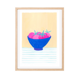 A framed original gouache artwork featuring a still life illustration of pink tomatoes in a blue bowl, set against a pale yellow background with light blue horizontal lines at the bottom. The original piece is styled with a white mat and a light natural wood frame.