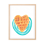 A framed original artwork featuring a heart-shaped waffle in yellow ochre and burnt sienna tones, layered over teal concentric circles on a white background, enclosed in a light natural wood frame.