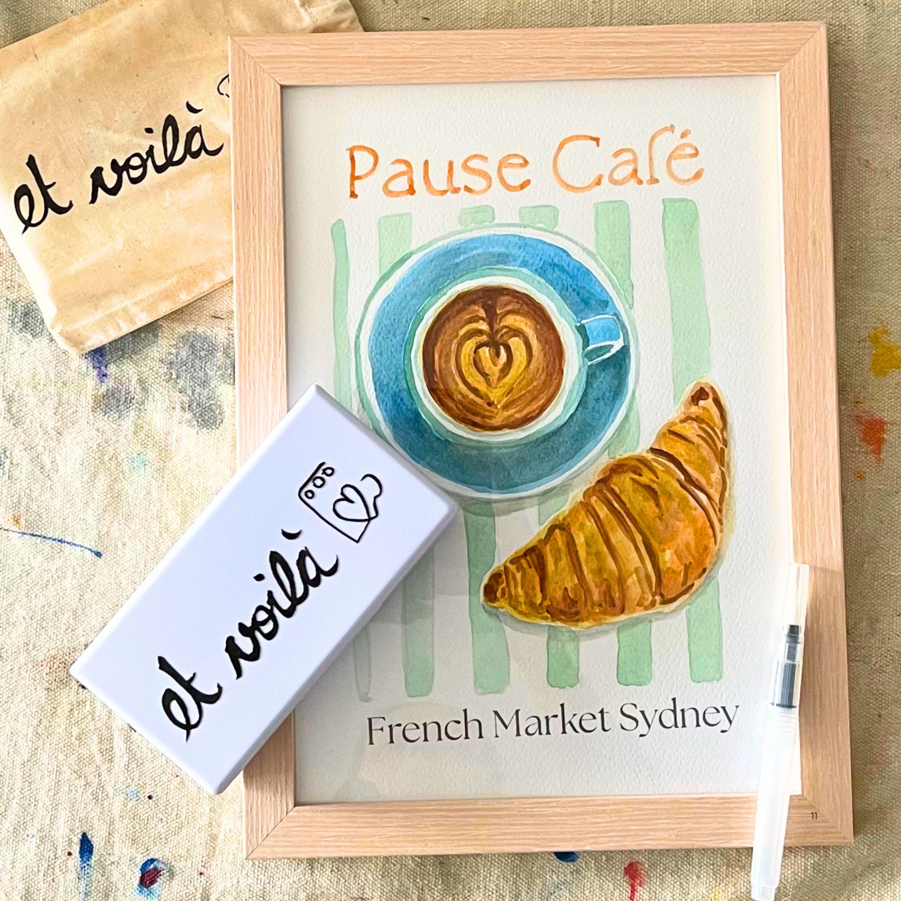 Framed artwork of a coffee cup and croissant with 'Pause Cafe' text, placed on a textured surface.