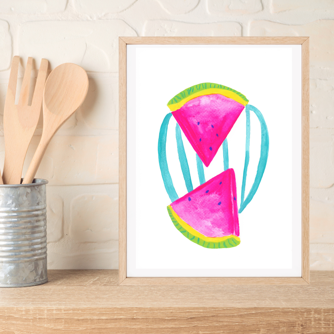 A framed original gouache painting featuring two pink watermelon slices with green rinds and teal stripes, displayed on a wooden shelf next to kitchen utensils against a white brick wall.