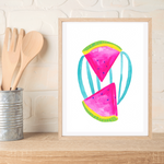 A framed original gouache painting featuring two pink watermelon slices with green rinds and teal stripes, displayed on a wooden shelf next to kitchen utensils against a white brick wall.