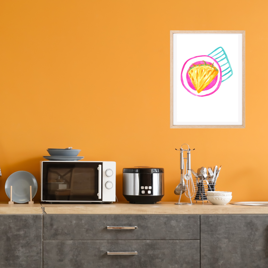 A framed original wall art featuring a colourful illustration of a pineapple slice on a pink plate and striped turquoise napkin displayed on a bright orange kitchen.