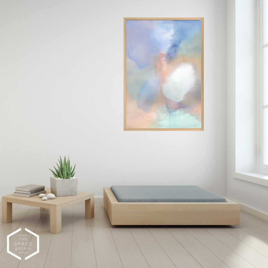 An abstract framed wall art print hangs on a white wall in a minimalist room setting with a light wood platform bed, a low wooden side table, and a small potted succulent.