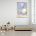An abstract framed wall art print hangs on a white wall in a minimalist room setting with a light wood platform bed, a low wooden side table, and a small potted succulent.