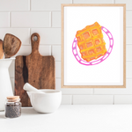A framed original gouache artwork featuring a colourful illustration of a waffle on a pink plate, displayed on a kitchen counter next to wooden cutting boards and a white bowl.